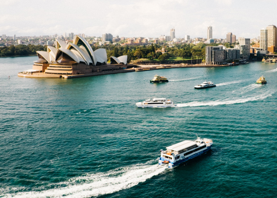 Some boats glide through the water near the Sydney Opera House, highlighting the famous landmark against the skyline.