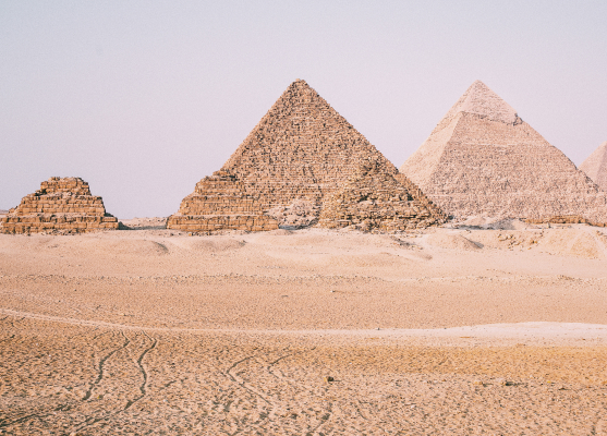Three large pyramids stand majestically in a vast desert landscape under a clear blue sky.