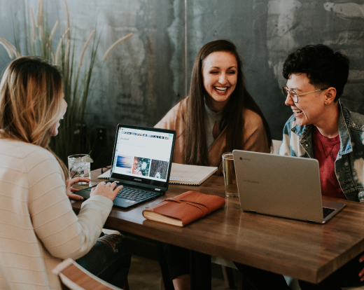 Three people are sitting at a table, doing their work and chatting a little.