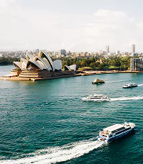 Some boats glide through the water near the Sydney Opera House, highlighting the famous landmark against the skyline.
