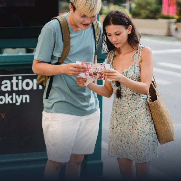 A man and a woman stand together on a street corner staring at a paper