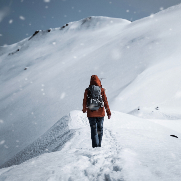 A woman walking uphill through a snowy landscape, leaving footprints in the fresh snow.